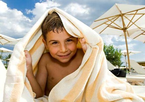 Niño bajo una toalla en una playa soleada