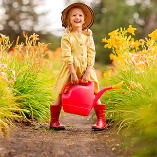 Niño con impermeable amarillo y botas de lluvia rojas, sosteniendo una regadera