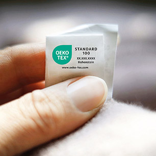 Mano sosteniendo un textil con la etiqueta cosida OEKO-TEX® STANDARD 100