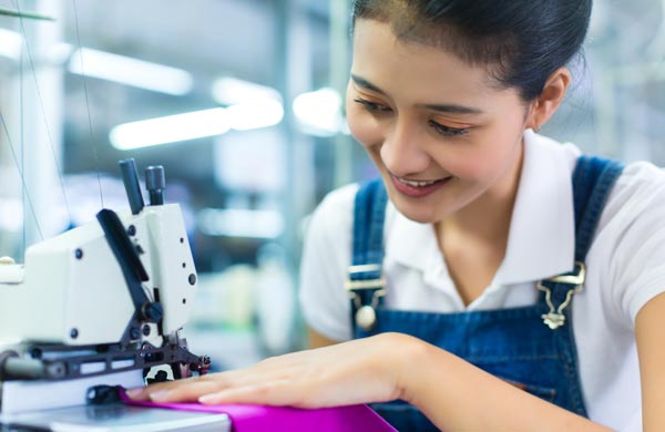 Trabajadora textil en máquina en coser en lugar en trabajo seguro