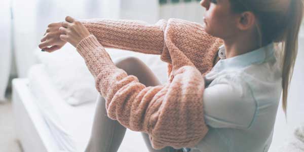 Mujer poniéndose un suéter mientras está sentada en una cama