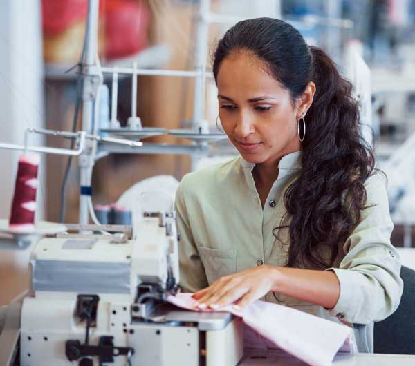 Trabajadora textil en fábrica de corte y costura cosiendo una prenda