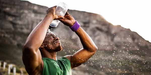 Corredor con camisa verde, vertiendo agua sobre su cabeza para refrescarse