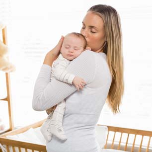 mamá sosteniendo recién nacido cerca de la cuna