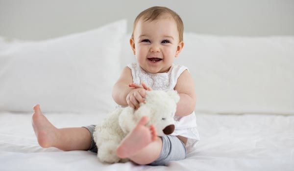 Bebé sosteniendo un animal de peluche en la cama