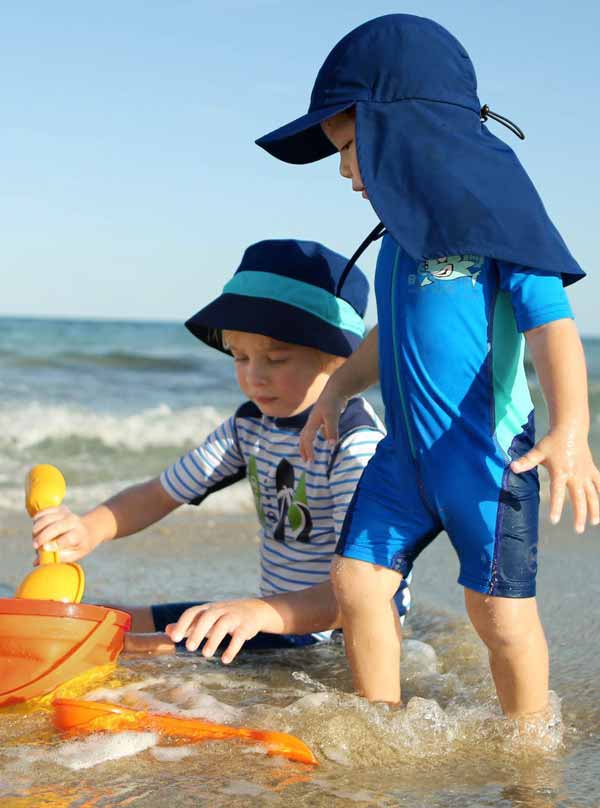 dos niños con ropa de protección UV, jugando en una playa soleada